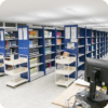 Imagem mostrando corredores de estantes de livros. As estantes são azuis.