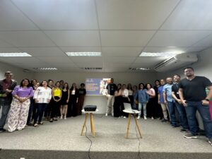 Fotografia colorida mostrando parte do público participante do evento. As pessoas estão de pé, no palco e ao fundo aparece imagem indicando ser o II encontro da Estatuinte.