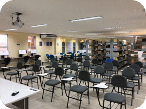 Foto colorida mostrando frontalmente parte do espaço da Labib. Em primeiro plano aparecem várias cadeiras escolares com estofado preto e ao fundo aparecem algumas estantes de açõ.