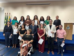 Foto colorida mostrando grupo de pessoas composto majoritariamente por mulheres. O grupo está alinhado em duas fileiras sorrindo para a câmera.